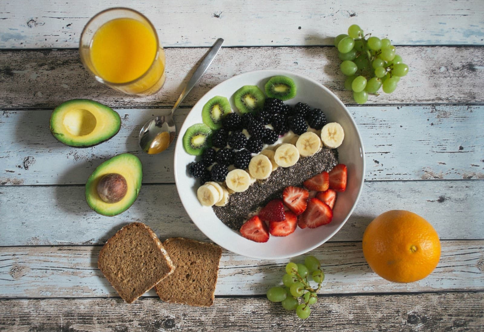 Ontbijt met yoghurt, kiwi, bramen, banaan en aardbei naast avocado en volkorenbrood — koolhydraten samen met vezels en gezonde vetten.